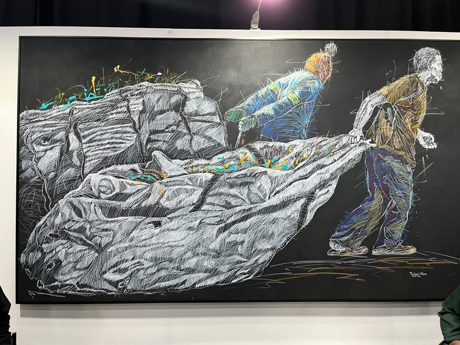Large monochrome artwork of figures hauling a rock-like form, with small bursts of colour pinned across the surface